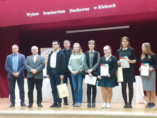 Uczestnicy konkursu stoją na schodach wraz z organizatorami i komisją egzaminacyjną