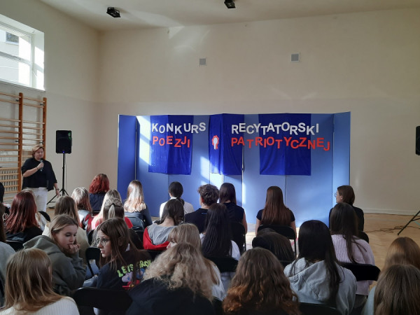 Pani Dyrektor przemawia na otwarciu konkursu recytatorskiego, w tle widnieje napis Konkurs Recytatorski Poezji Patriotycznej.