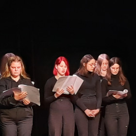 Na scenie teatru młodzież czyta Antygonę.