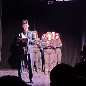 Na scenie teatru młodzież czyta Antygonę. Kreon stoi z przodu.