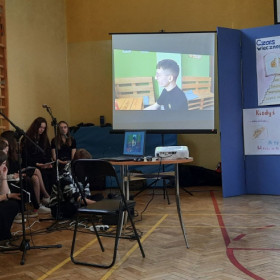 Uczniowie siedzą przy drabinkach w sali i oglądają film.