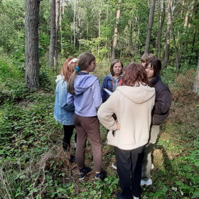 Młodzież stoi w lesie i rozwiązuje zadanie