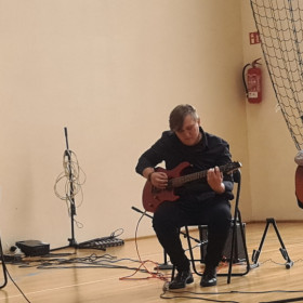 Dwie osoby grają na gitarach, uczennica śpiewa.