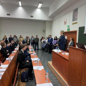 Uczniowie siedzący na auli słuchają przemowy organizatora.