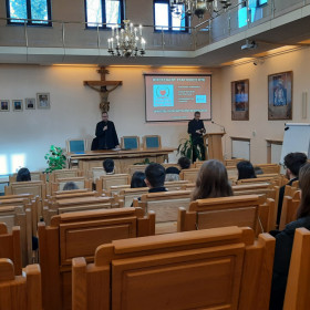 Widok auli, uczestnicy konkursu siedzą, ksiądz przemawia.