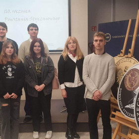 Uczniowie z klasy IIIf wraz z opiekunem na tle plansz prezentującym monety kolekcjonerskie wyemitowane przez NBP z okazji 160 rocznicy wybuchu powstania styczniowego.