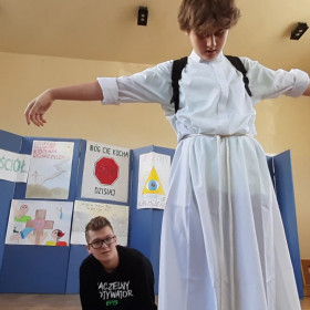 Chłopak odgrywający rolę Jezusa stoi w postawie ukrzyżowanego.
