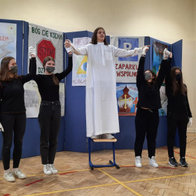 Osoby przedstawiając pantomimę stoja w rzędzie, jedna osoba stoi na krzesle.