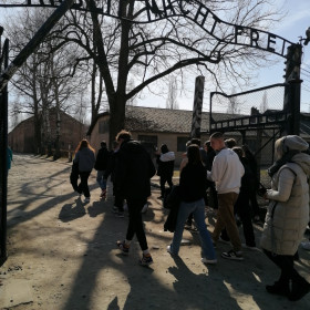 Uczniowie przechodzą pod bramą z napisem Arbeit macht frei.