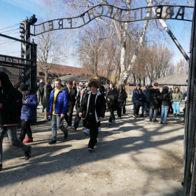 Uczniowie przekraczają bramę z napisem Arbeit macht frei.