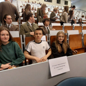 Na auli siedzą uczniowie, kartka z napisem VII Liceum Ogólnokształcace im. Józefa Piłsudskiego w Kielcach.
