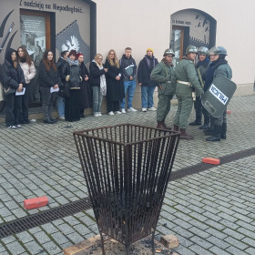 Uczniowie oglądają pokazy grupy rekonstrukcyjnej w strojach MO i ZOMO. W tle widoczny koksownik