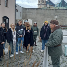 Uczniowie oglądają pokazy grupy rekonstrukcyjnej w strojach MO i ZOMO. W tle widoczny koksownik