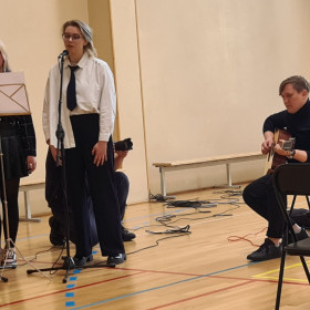 Uczennice śpiewają, nauczyciel gra na gitarze.
