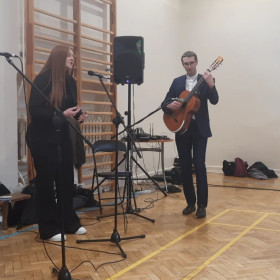 Dziewczyna śpiewa solowo kolędę, ksiądz gra na gitarze