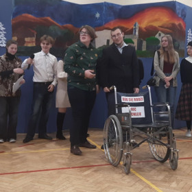 Osoby na scenie, chłopak wiezie wózek szpitalny