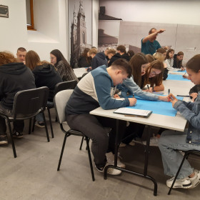 Uczestnicy warsztatów siedzący przy stołach i przygotowujący plakaty