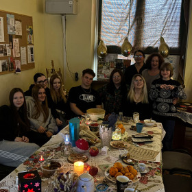 grupa uczniów z nauczycielami siedząca przy stole podczas wieczorku poetyckiego