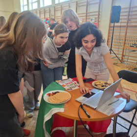 Wolontariuszka pokazuje grupie uczniów zadanie, wyświetlone na monitorze laptopa.