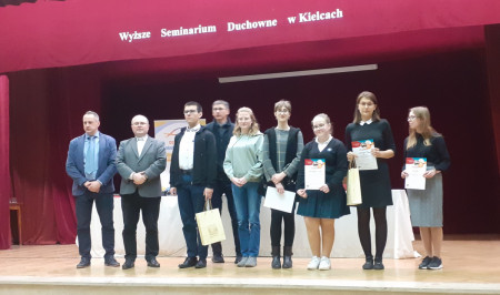 Uczestnicy konkursu stoją na schodach wraz z organizatorami i komisją egzaminacyjną