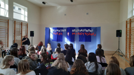 Pani Dyrektor przemawia na otwarciu konkursu recytatorskiego, w tle widnieje napis Konkurs Recytatorski Poezji Patriotycznej.
